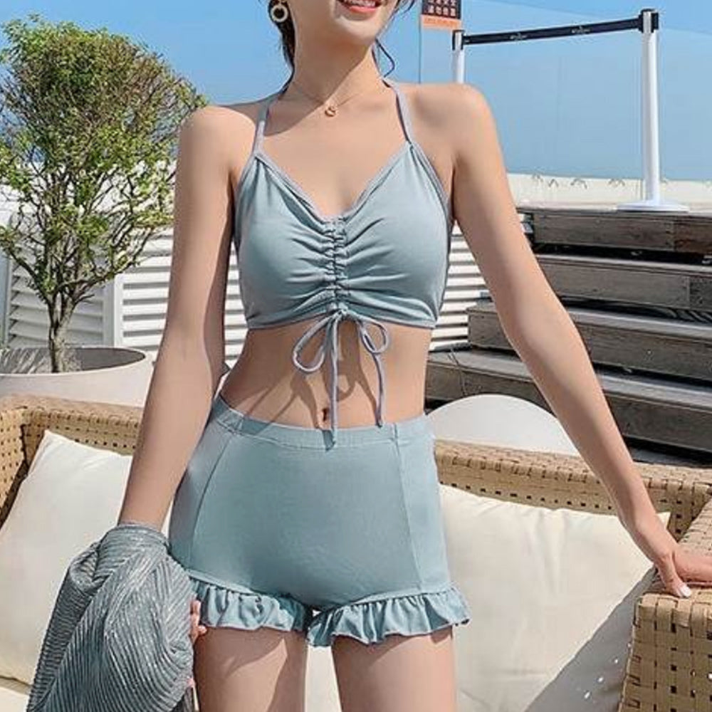 青い水着セットを着た女性が屋外のデッキチェアに座る写真。胸元にギャザーが入ったトップスと、裾にフリルが付いたショートパンツが特徴